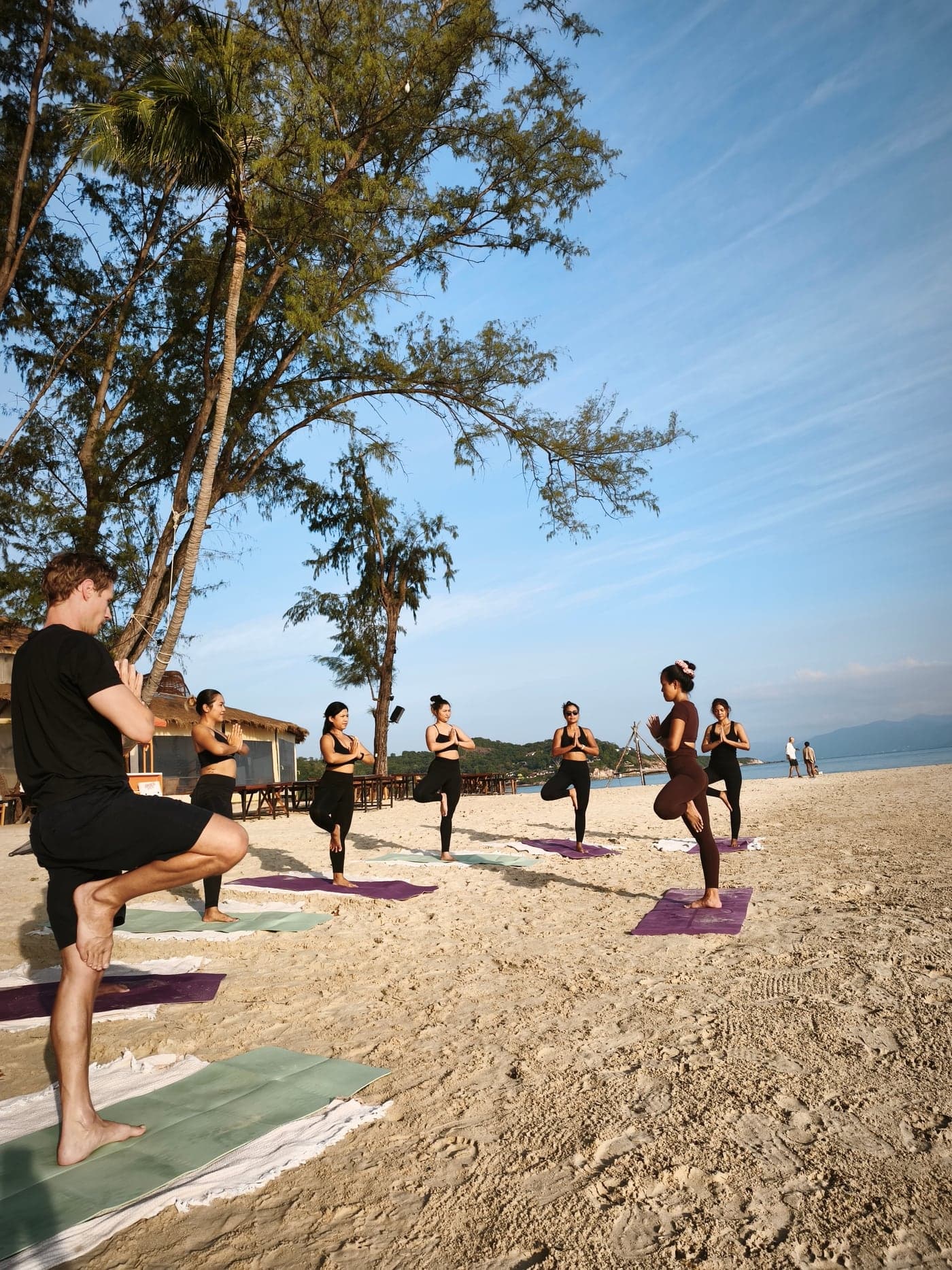 A group practising yoga together on the beach in Koh Samui